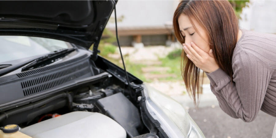 車のボンネットを開けて口に手をあてる女性