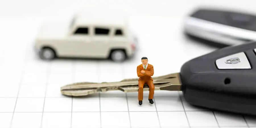 車のキーに座り腕組みをする人形
